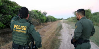 Two U.S. Border Patrol officers standing on a dirt path.