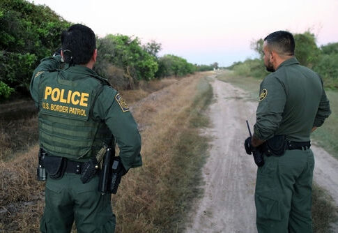 Two U.S. Border Patrol officers standing on a dirt path.