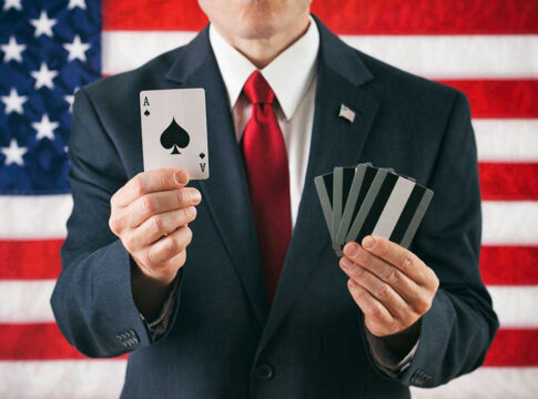 Man in suit holding ace of spades and cards.