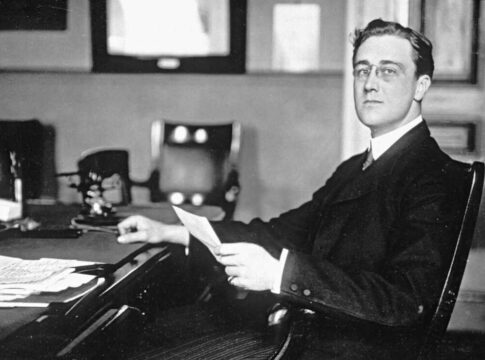 President Franklin Roosevelt seated at a desk in a formal setting, holding a document