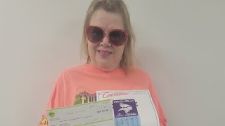 Woman wearing sunglasses holding a scratch-off ticket and a check