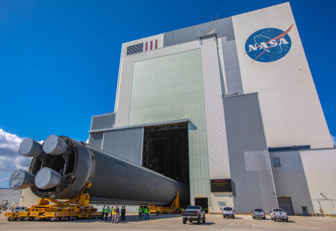 A large rocket being transported outside a NASA building under a blue sky