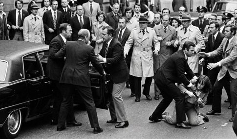 A chaotic scene with a crowd surrounding a car and individuals in a struggle