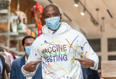 Man wearing Vaccine and Testing hoodie, pointing at text.