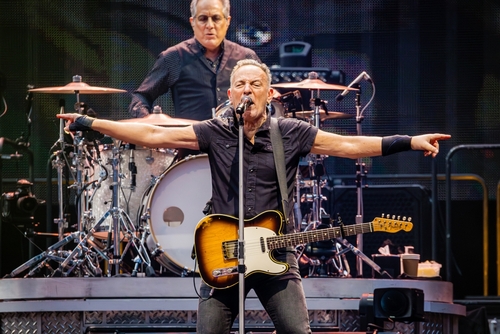 A guitarist performing passionately on stage with a drummer in the background