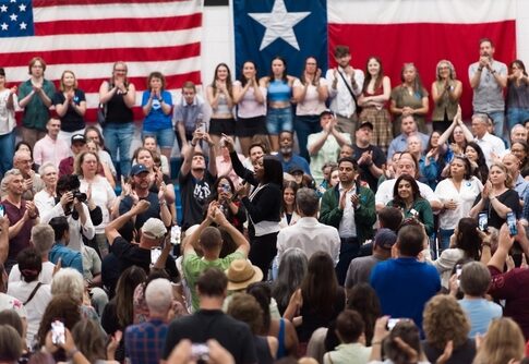 A large crowd at a political rally with people cheering and taking photos