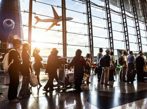People queuing inside airport terminal with airplane flying outside.