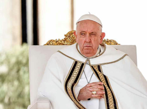 Elderly man in white robe sitting on chair.
