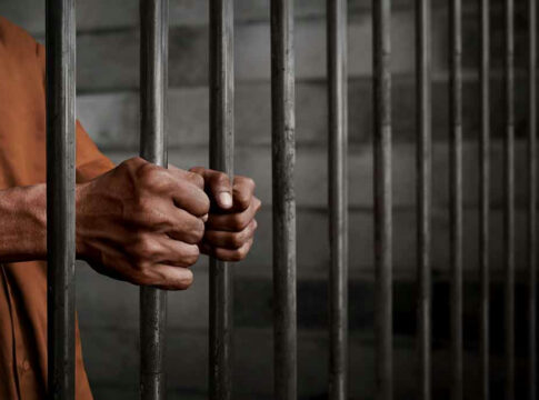 Hands gripping prison cell bars tightly.
