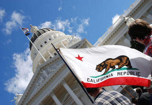 California state flag waving near a white domed capitol building