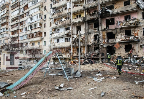 Damaged apartment building with debris scattered firefighters present.