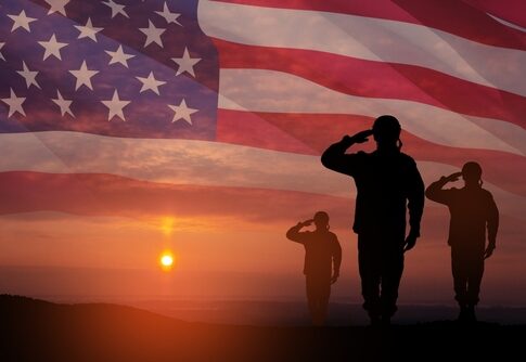 Silhouetted soldiers saluting against an American flag backdrop during sunset