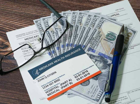 Medicare card with cash, documents, glasses, and pen.