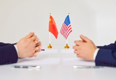 Two hands of individuals facing each other with flags of China and the USA on the table