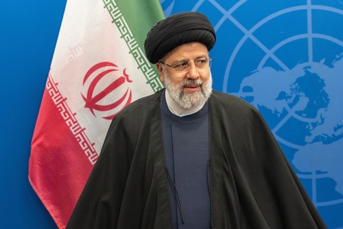 An Iranian political leader standing in front of the Iranian flag at a conference