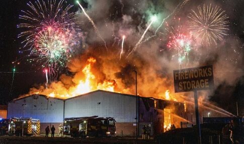 A large building engulfed in flames with fireworks in the sky