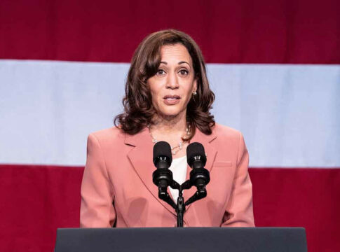 Woman speaking at podium with American flag background.